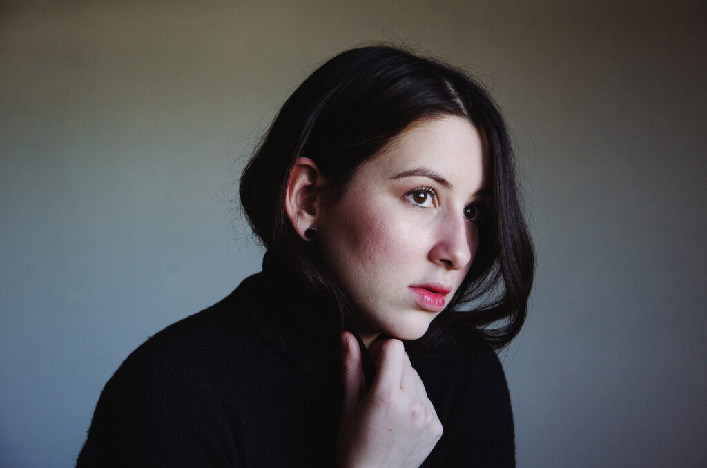 Gabriela Inzunza gazes into the distance her hand delicately touching her neck set against a muted background.